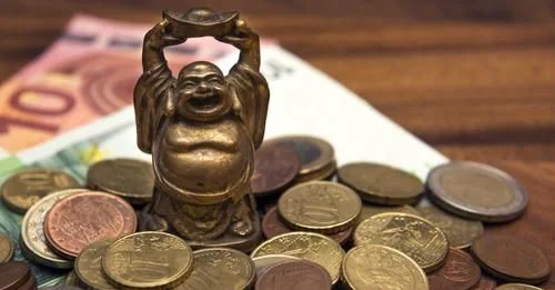 Une statuette de Bouddha rieur posée sur des pièces et des billets en euros