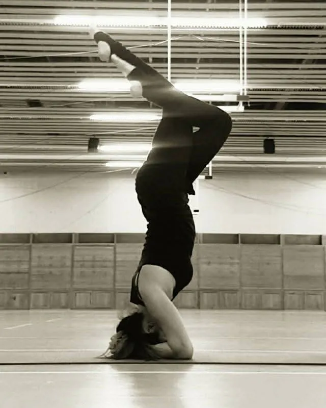 Helena Ona en équilibre sur la tête, jambes repliées, dans une salle de pratique