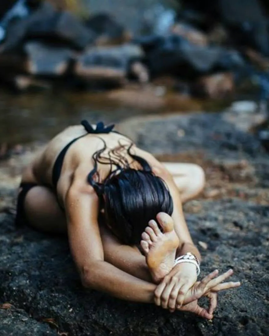 Helena Ona penchée en avant sur une jambe, assise sur un rocher au bord d'une rivière