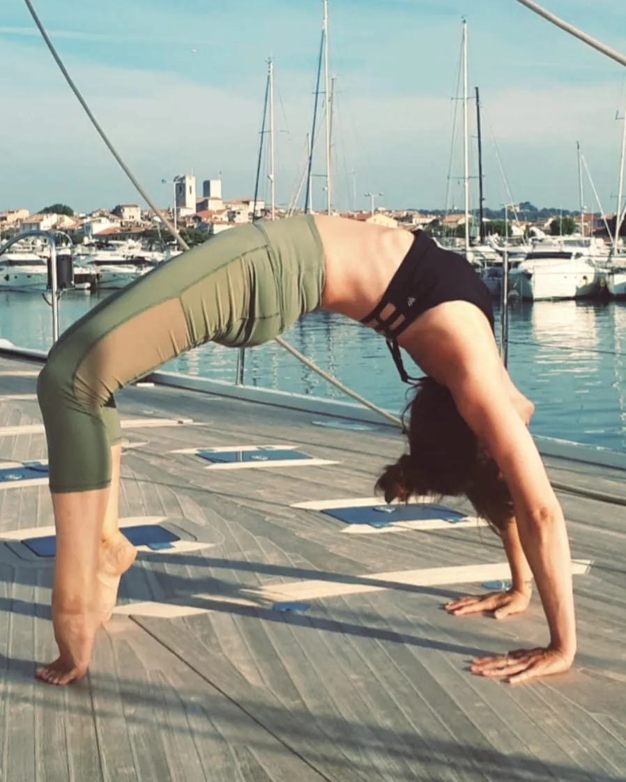 Helena Ona en posture de la roue sur le pont d'un voilier, dans un port de la Côte d'Azur