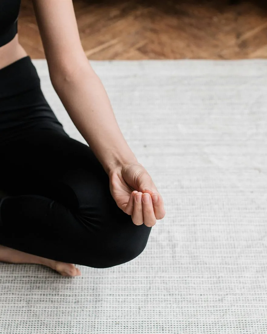 Une personne assise en tailleur sur un tapis, la main posée sur le genou