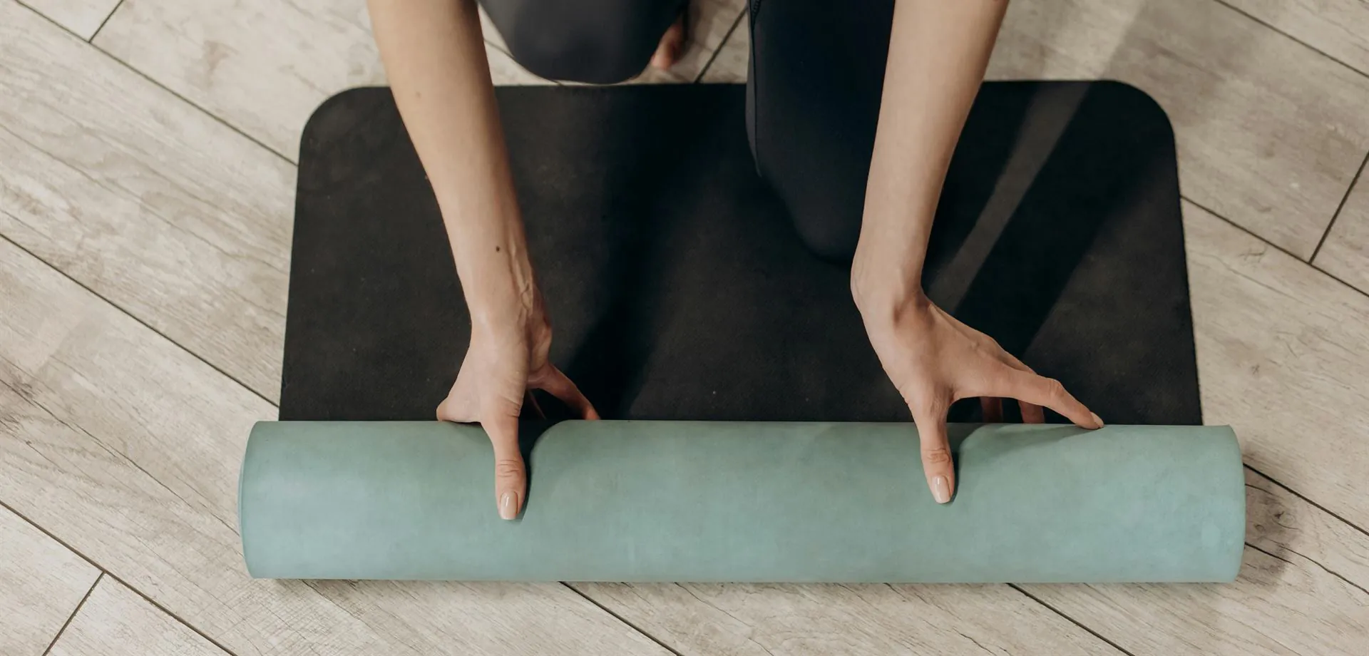 Une personne à genoux déroule un tapis de yoga sur un parquet