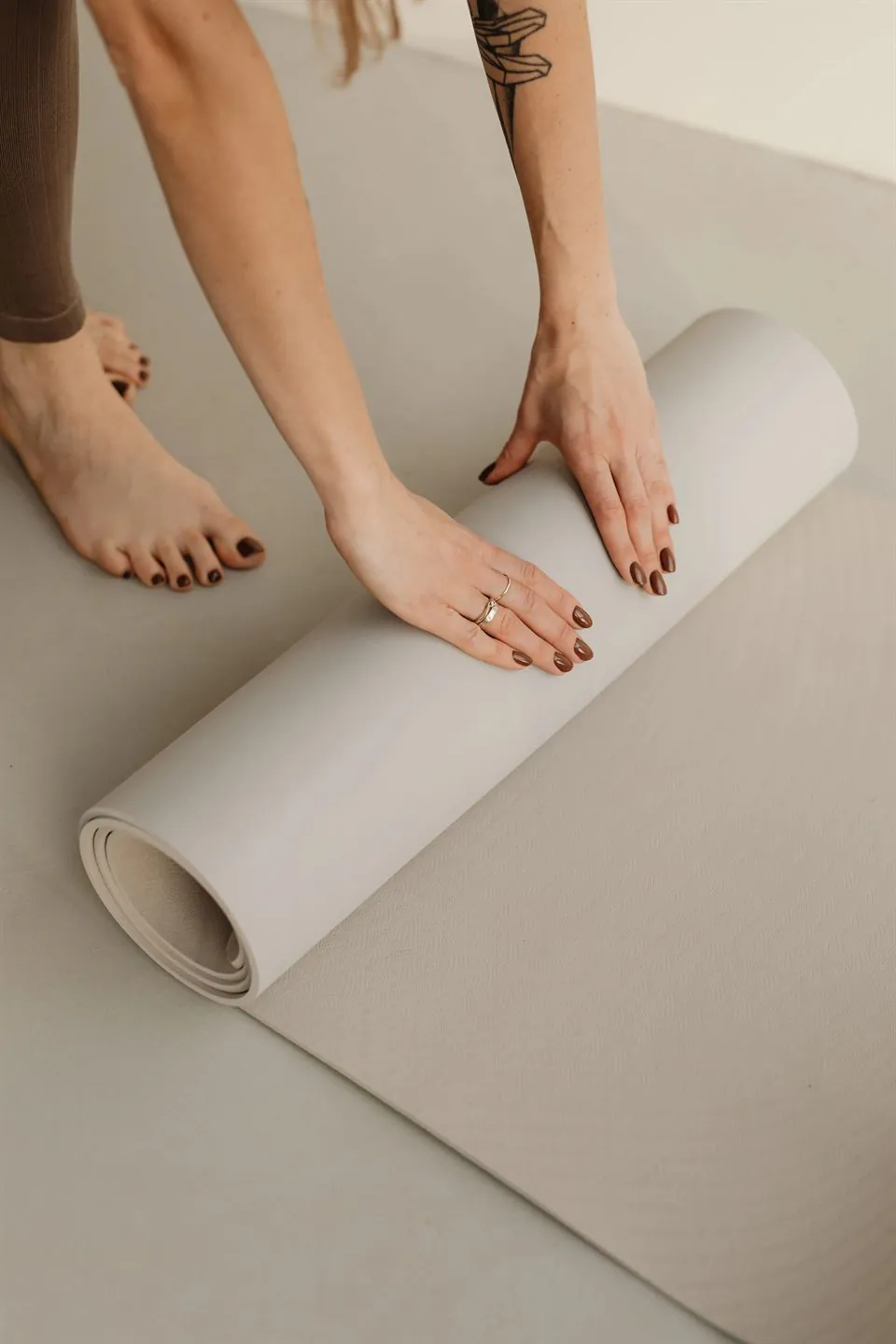Deux mains roulent un tapis de yoga gris clair, pieds nus posés à côté