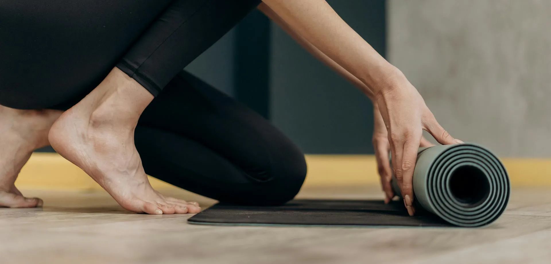 Une personne accroupie roule son tapis de yoga à la fin d'un cours